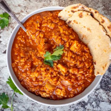 Bowl of chicken tikka masala with a side of naan and garnished with cilantro.