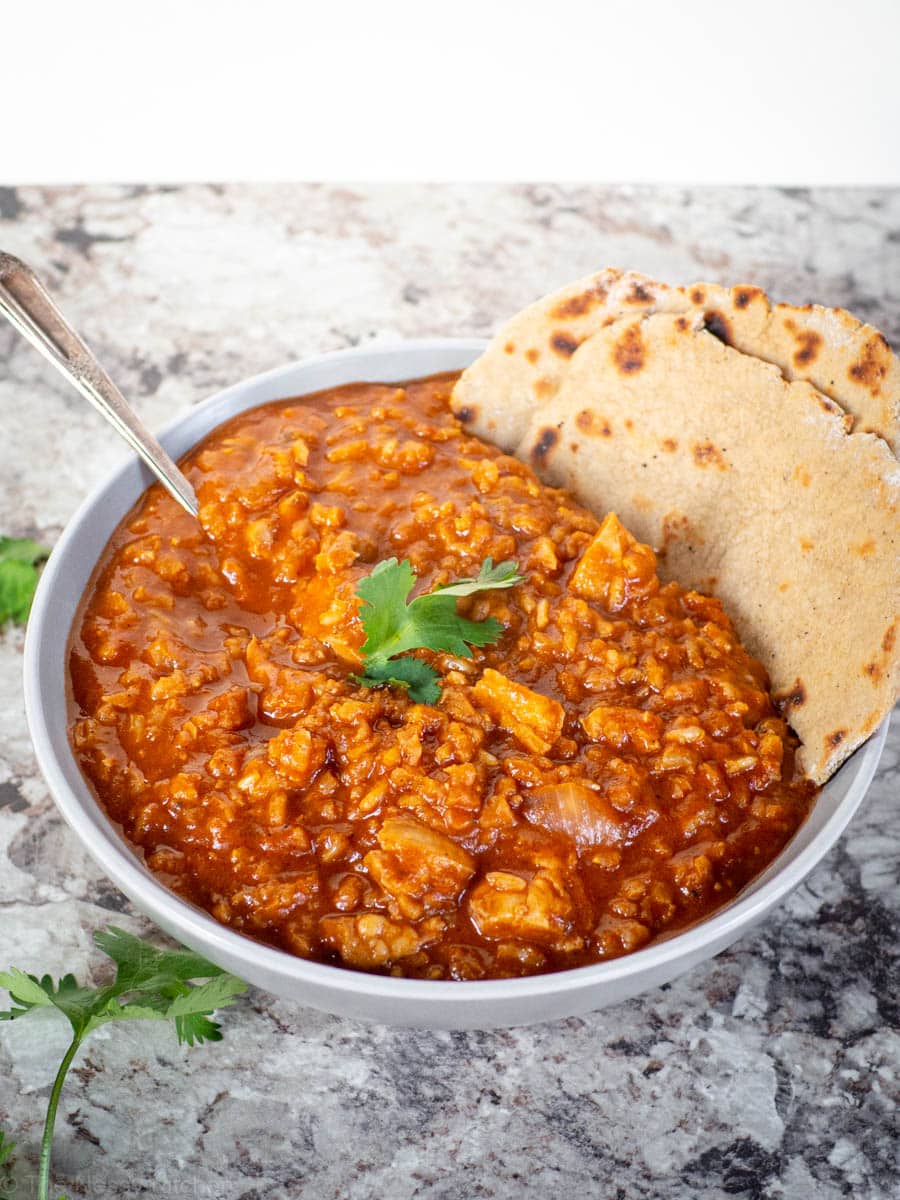 Bowl of chicken tikka masala with a side of naan.