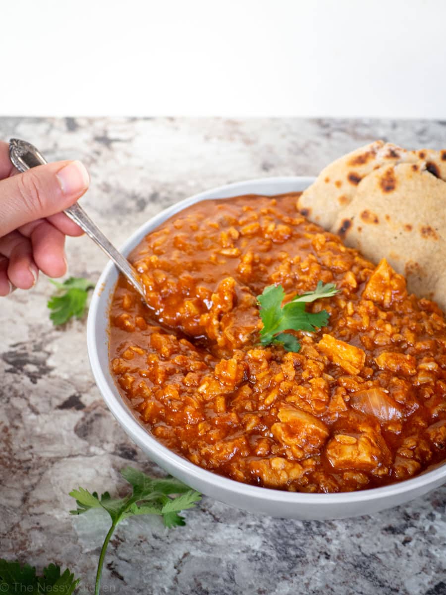 Hand taking a spoonful of Chicken tikka masala from a bowl.