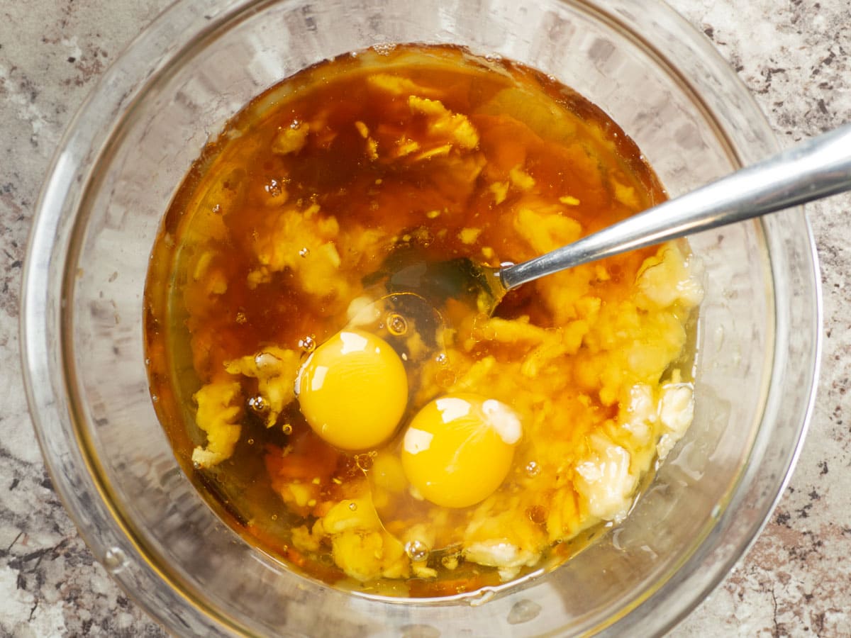 Mashed banana in a mixing bowl with other wet ingredients.