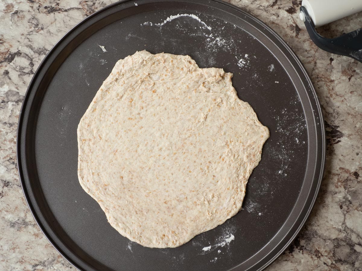 Pizza dough rolled out onto a pan.