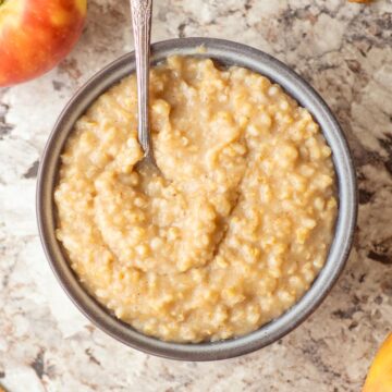 Bowl of oatmeal next to apples with a spoon.