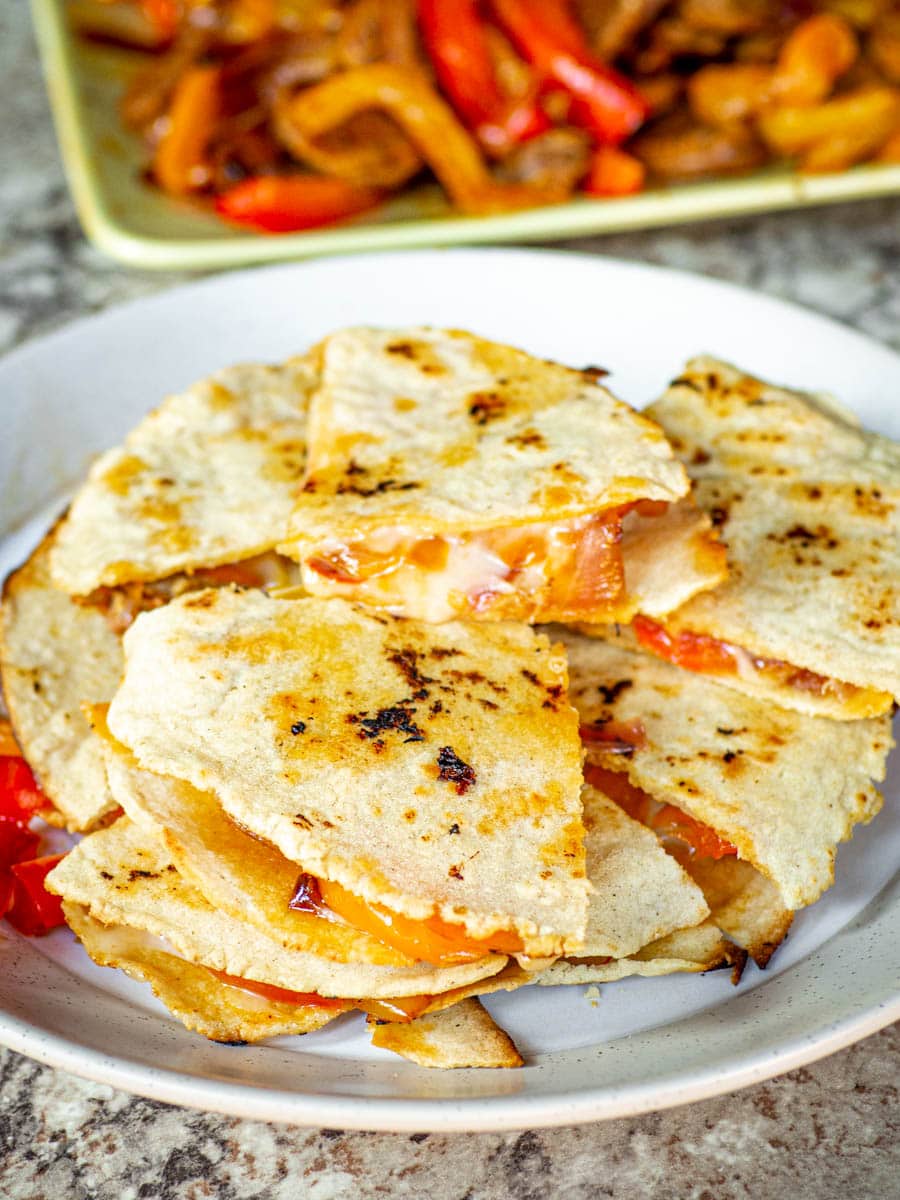 Quesadillas cut into quarters and stacked onto a heap on a plate with filling on a plate in the background.