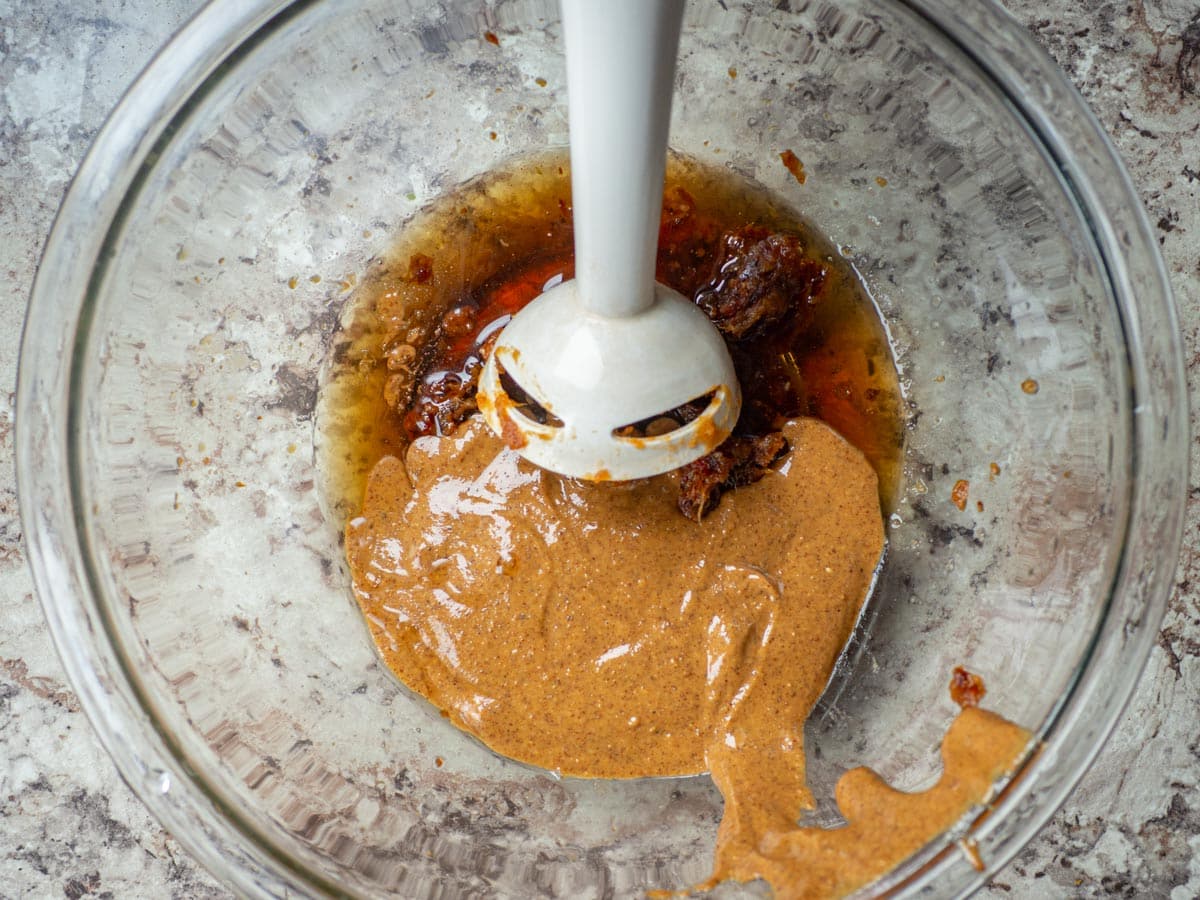 Almond butter, dates and syrup in a mixing bowl.