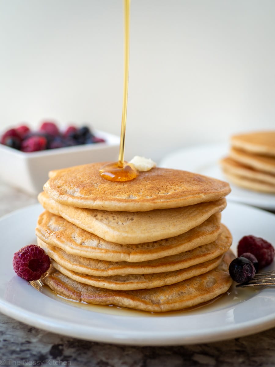 Syrup being poured onto a stack of pancakes.