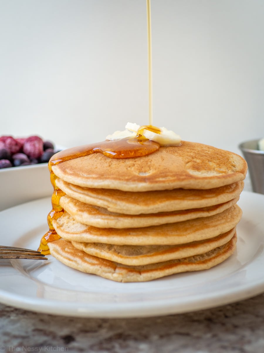 Oat flour pancakes on a plate with maple syrup drizzling down the side.