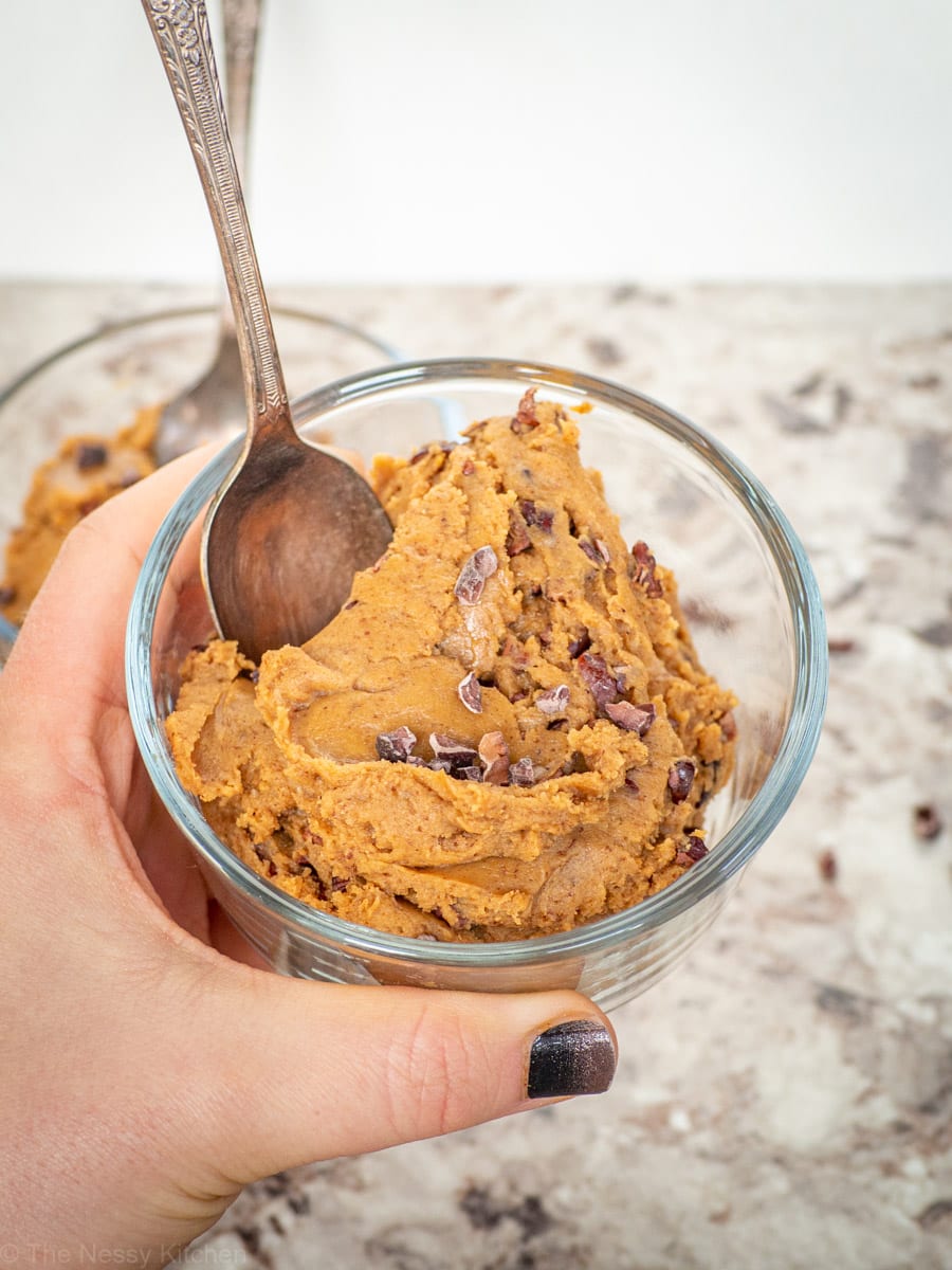 Hand holding up a bowl of cookie dough with a spoon.
