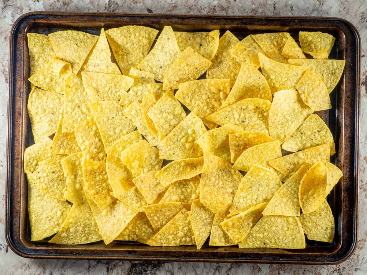 Tortilla chips spread out on a sheet pan.