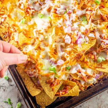 Hand taking a chip from a tray of nachos.