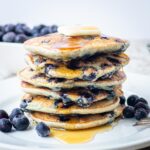 Blueberry pancakes on a plate topped with butter and syrup.