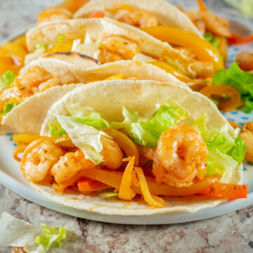 Shrimp taco filling in corn tortillas with lettuce and peppers.