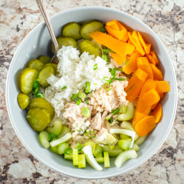 Tuna and rice in a bowl topped with pickles and fresh vegetables.