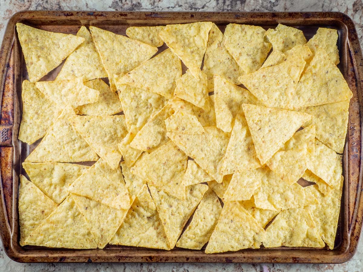 Tortilla chips spread out on a baking sheet.