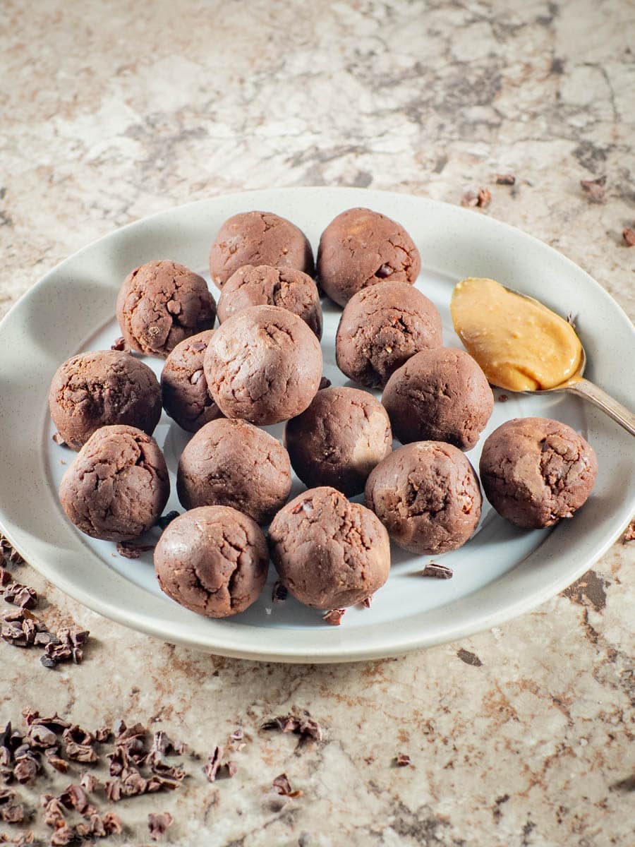 Protein balls on a plate with a spoonful of peanut butter.
