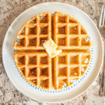 Waffle on a plate topped with butter and maple syrup.