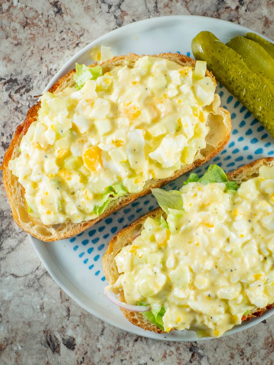 Open faced egg salad sandwich on a plate with pickles.