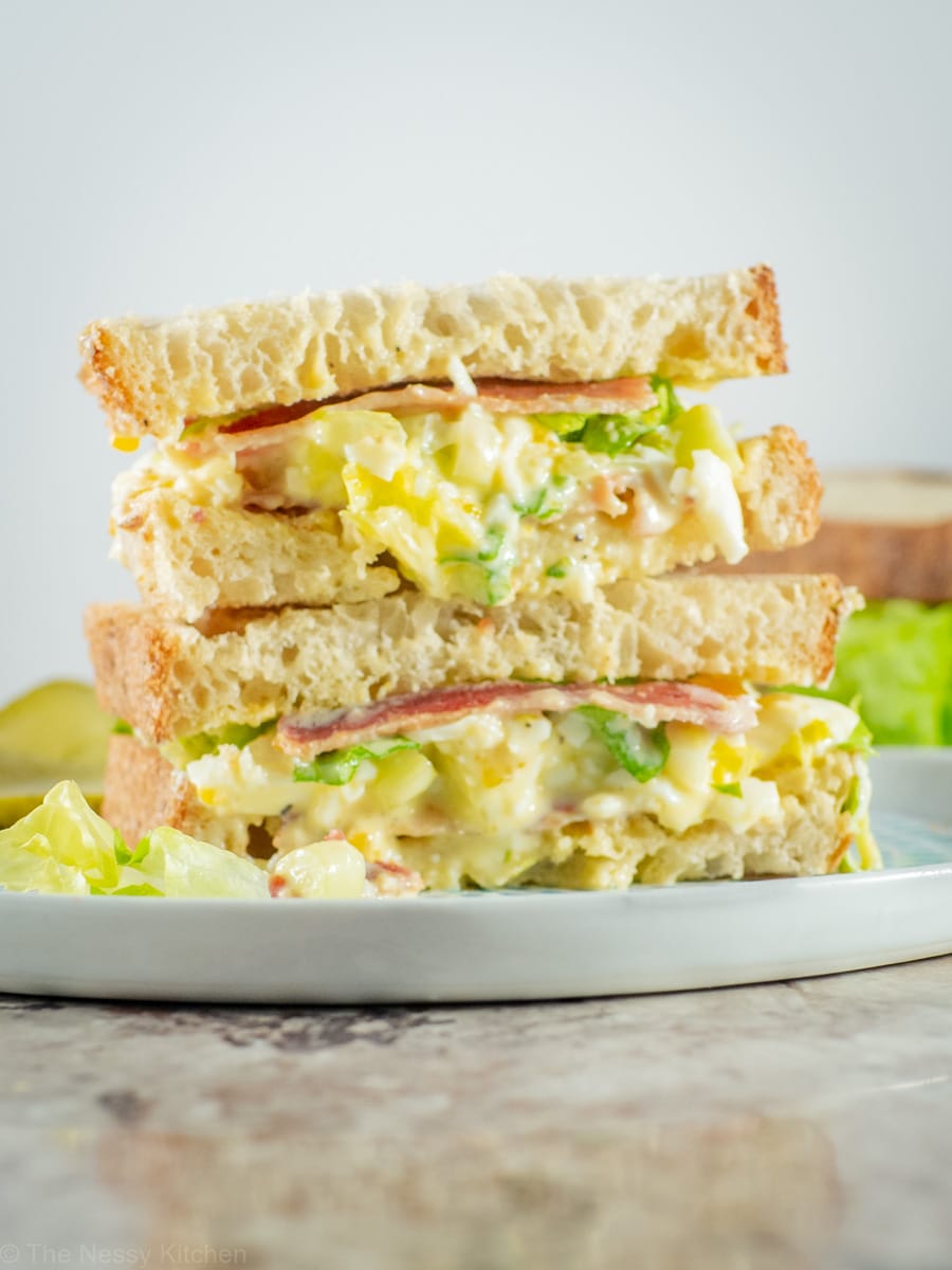 Egg salad sandwich sliced and stacked on a plate.