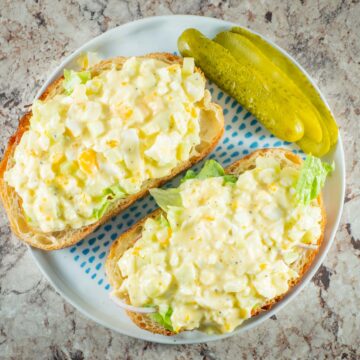 Open faced egg salad sandwiches on a plate with pickles.