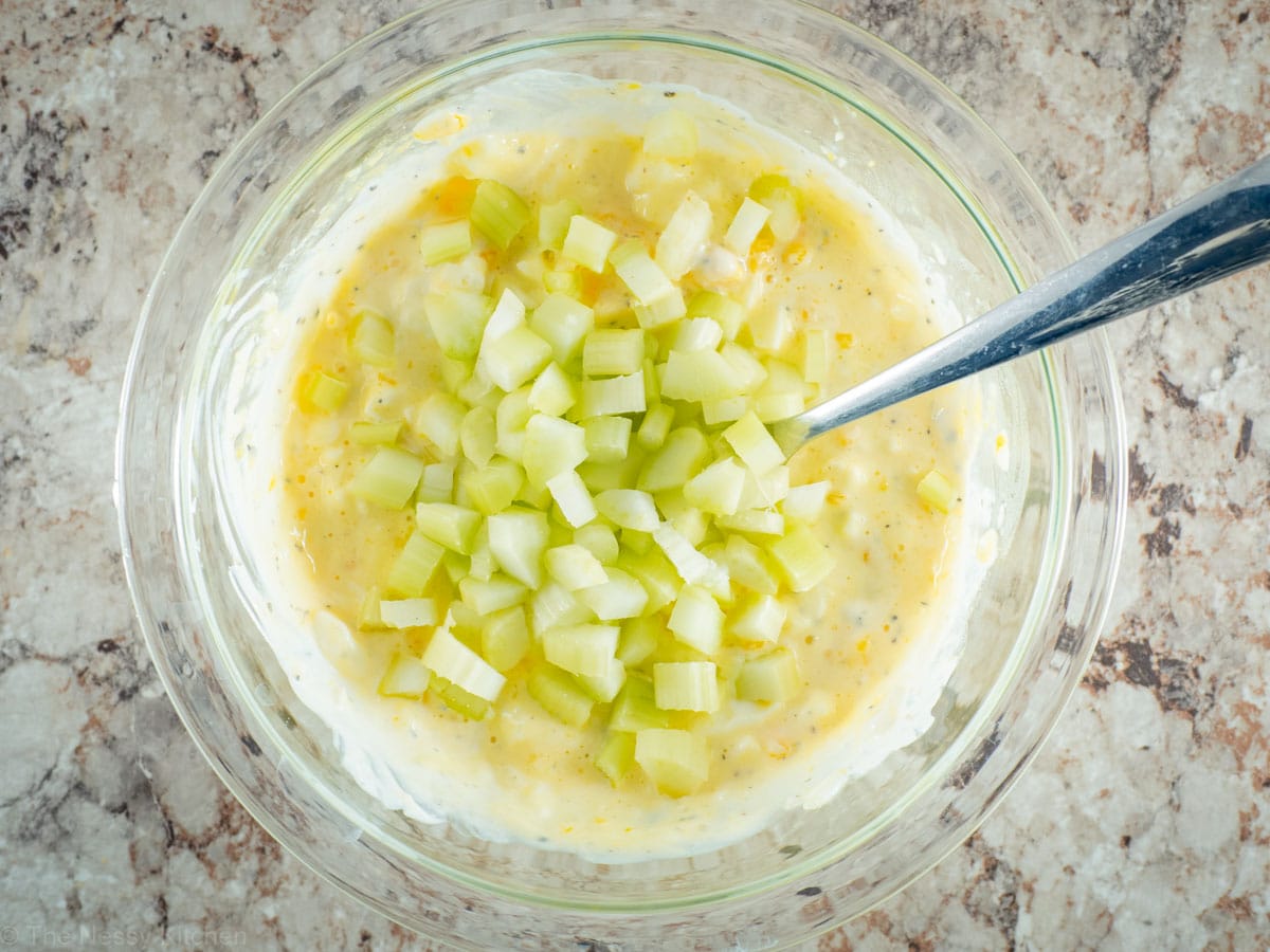 Celery added to a mixing bowl of egg salad.