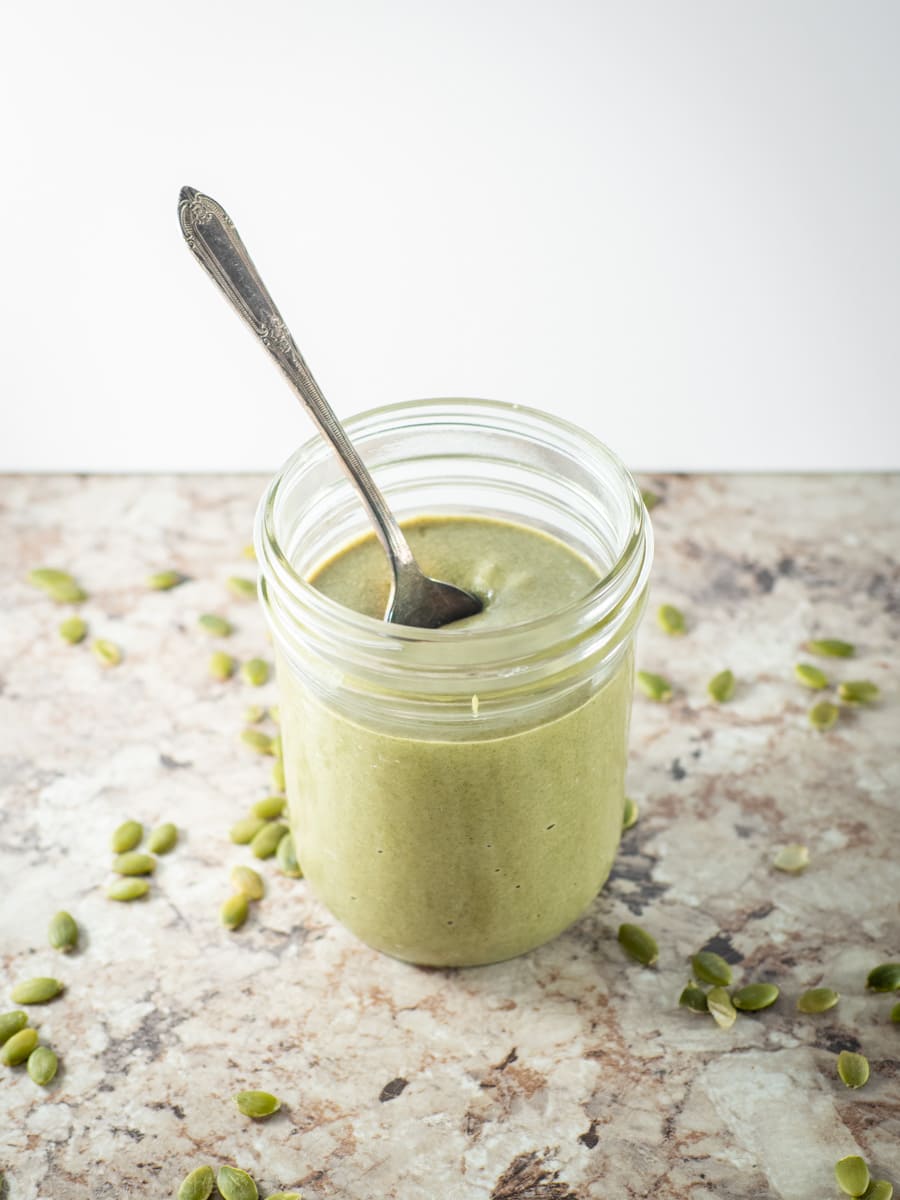 Jar of pumpkin seed butter with a spoon with pepitas on the counter alongside it.