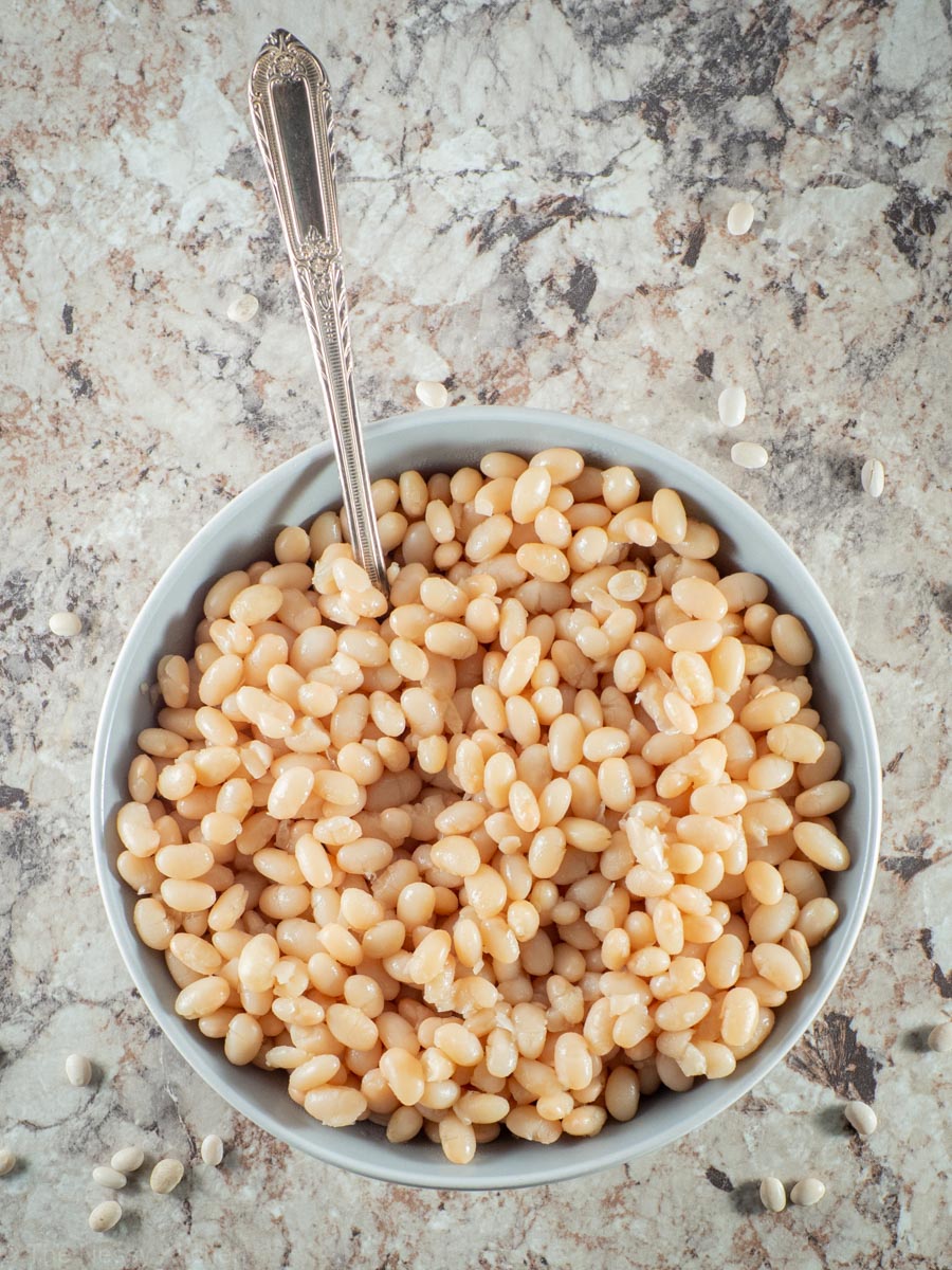 White beans in a grey bowl with a spoon.