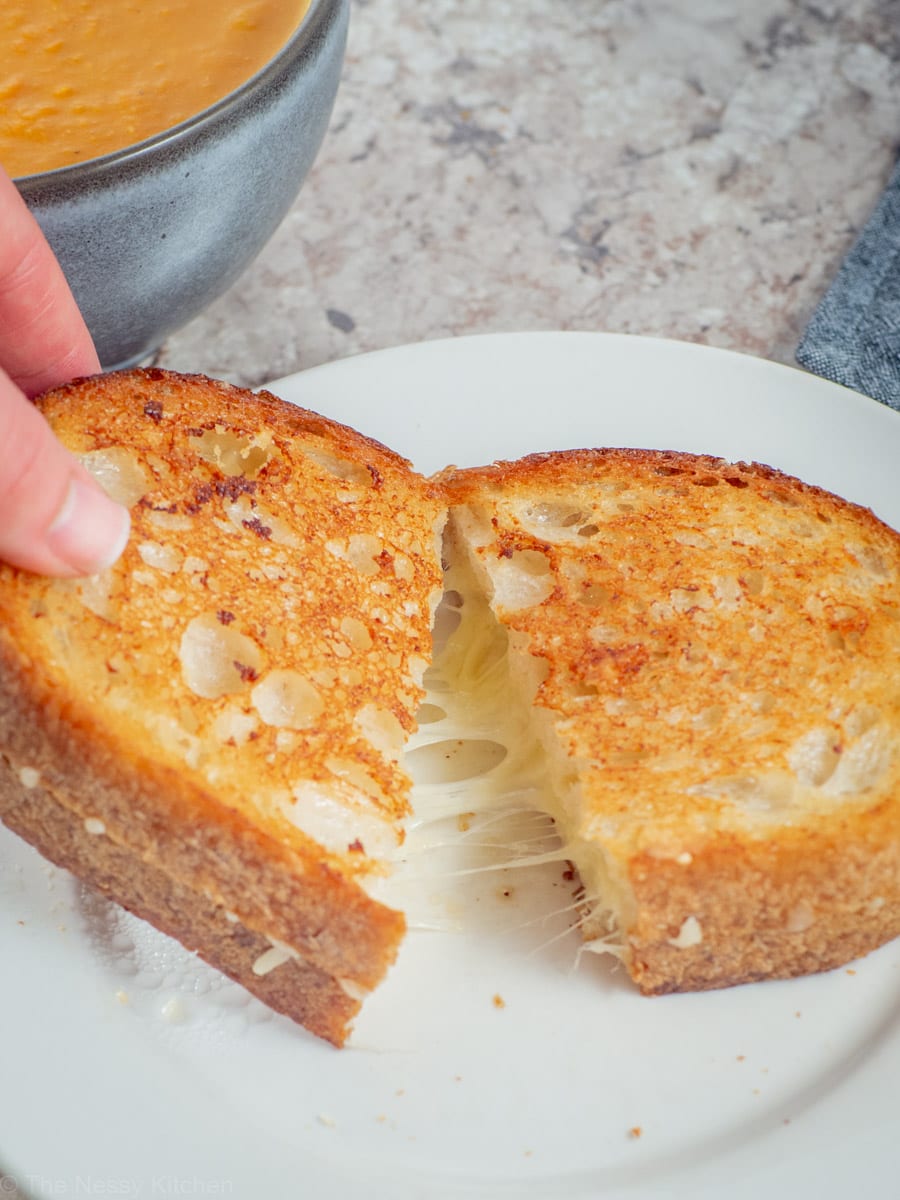 Hand pulling apart a sliced sourdough grilled cheese sandwich.