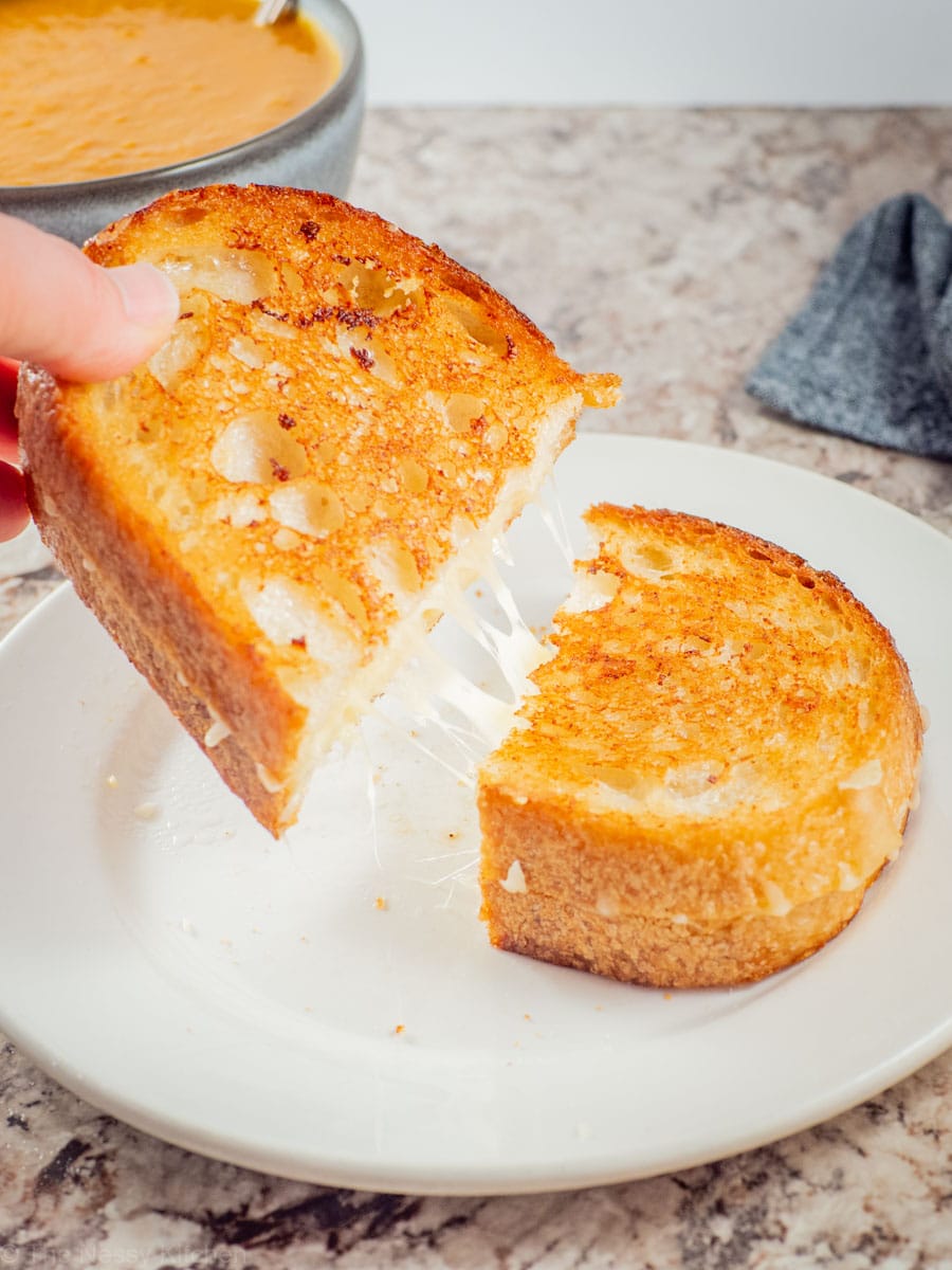 Hand pulling apart a grilled cheese sandwich.
