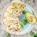 Baked fish tacos assembled with slaw and avocado on a plate.