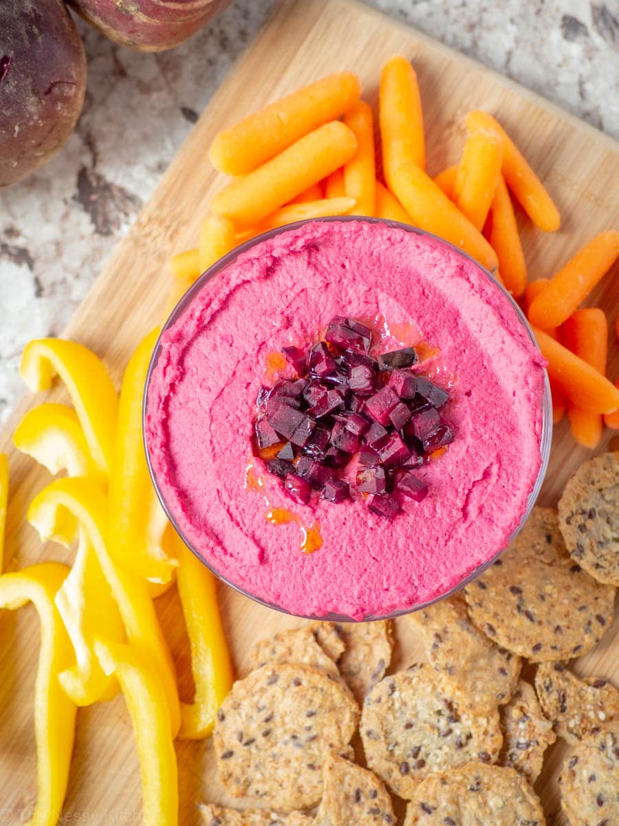 Beet hummus in a bowl surrounded by crudite.