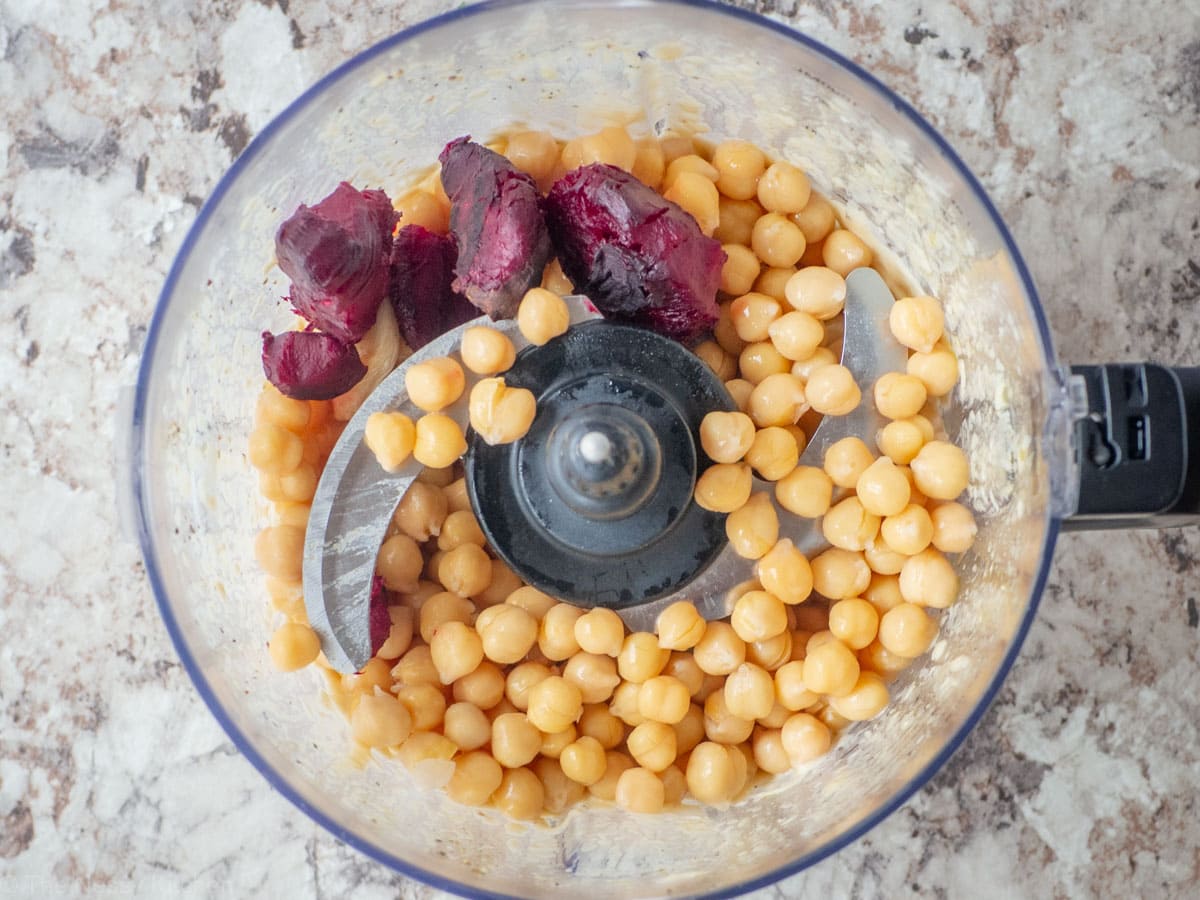 Beets and chickpeas added to the base of a food processor.