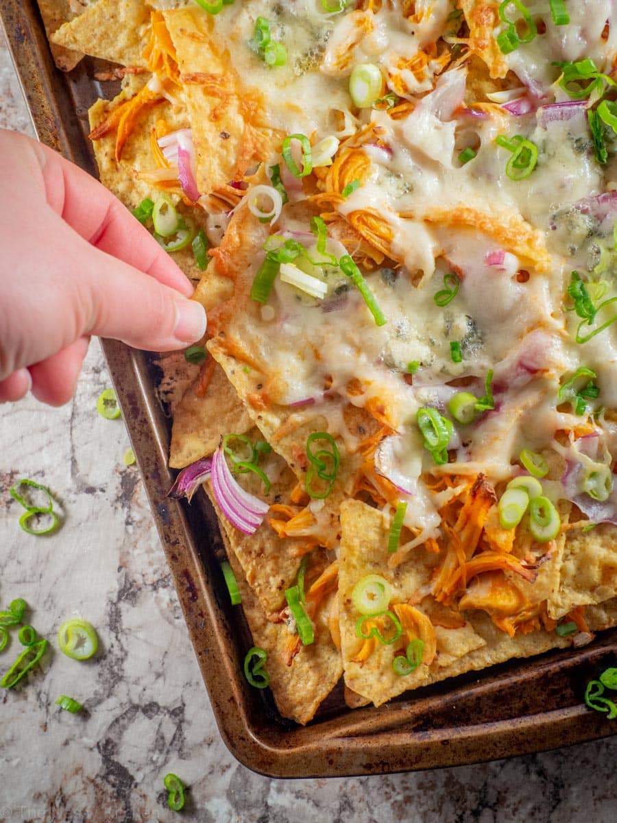 Hand taking a nacho from a sheet pan of buffalo chicken nachos.