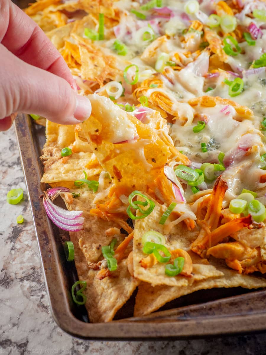 Hand taking a bite from a sheet pan of nachos.