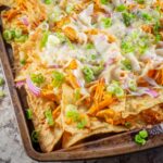 Chicken nachos on a sheet pan topped with green onions.
