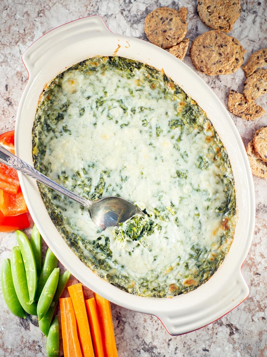 Warm spinach dip with cheese melted on top and a serving spoon.