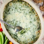 Warm spinach dip with cheese melted on top and a serving spoon.