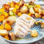 Pork chop on a plate surrounded by roasted vegetables.