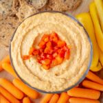 Red pepper hummus in a bowl topped with chopped roasted red peppers.