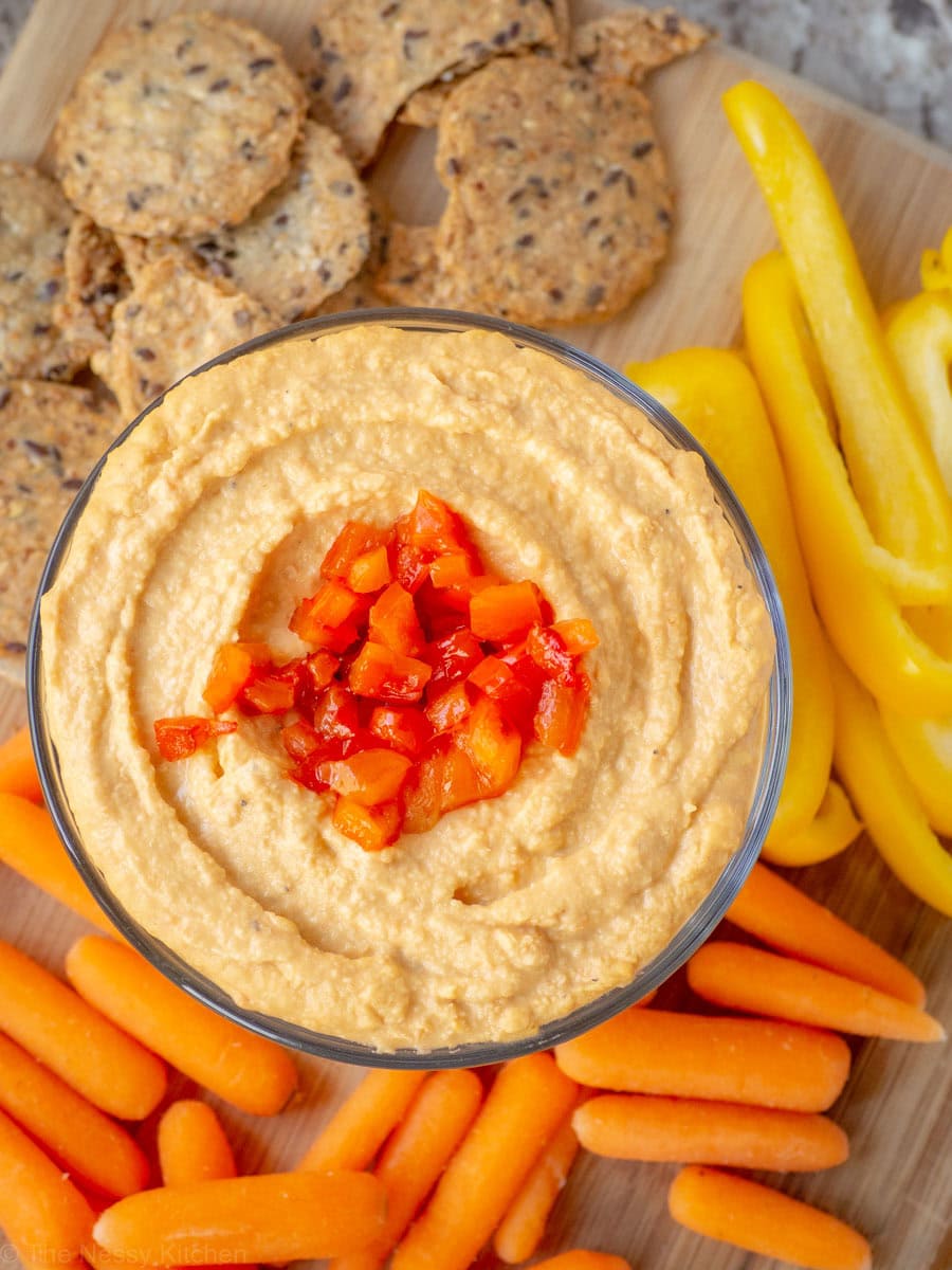 Red pepper hummus surrounded by a platter of crudite and crackers.