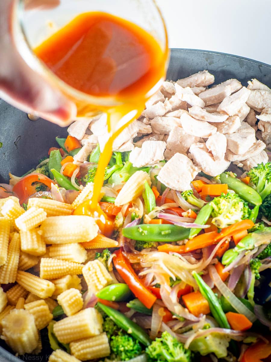 Sauce being poured over stir fry vegetables and chicken.