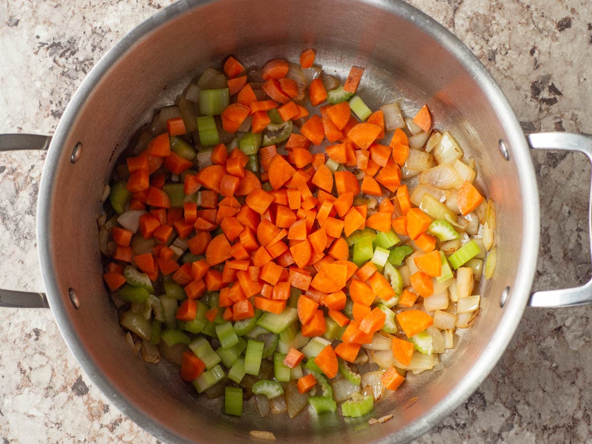 Carrots and celery added to a large pot with onions.