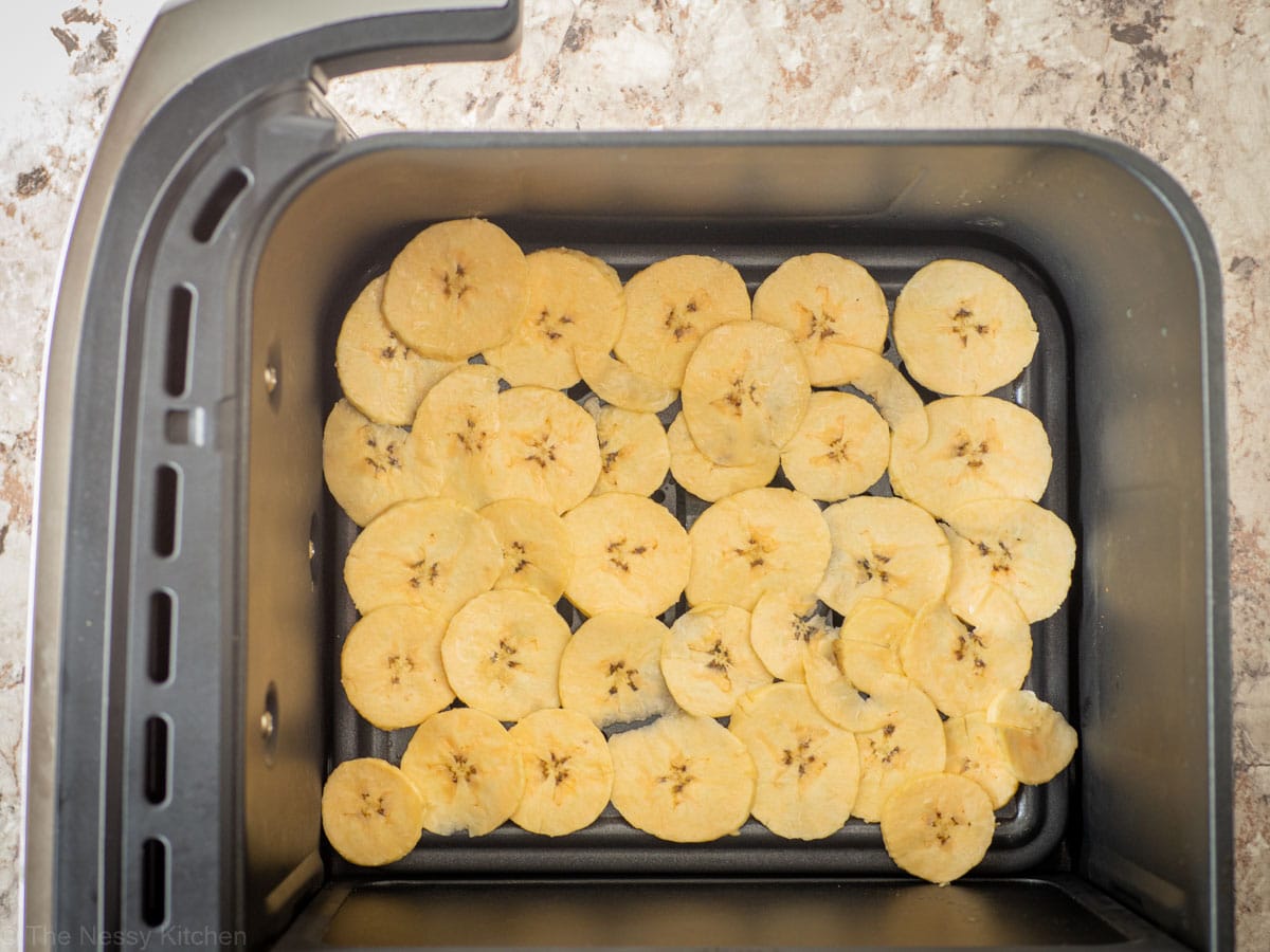 Sliced plantains in an air fryer basket.