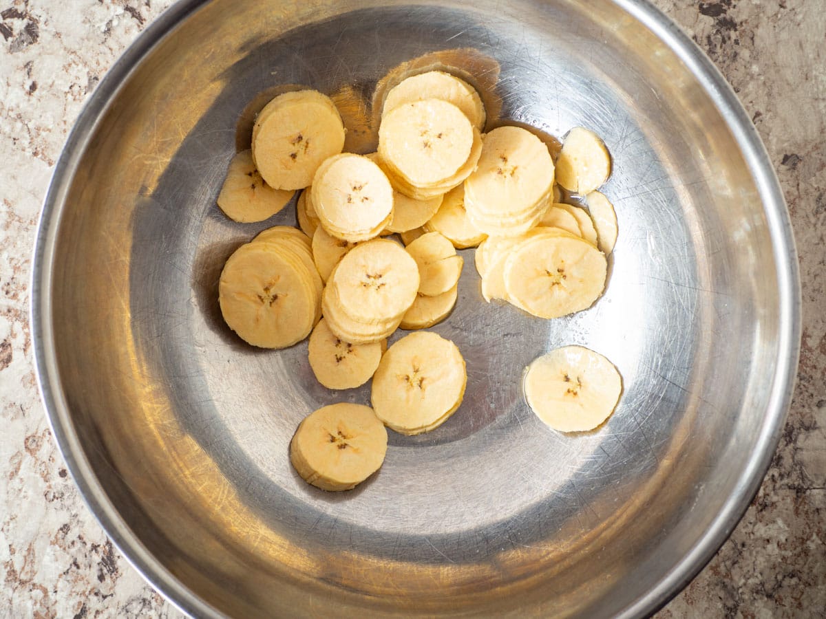 Sliced plantains in a bowl with salt and oil.