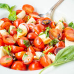 Caprese salad with cherry tomatoes and a spoon in a bowl.