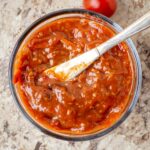 Tomato jam in a container with a knife.