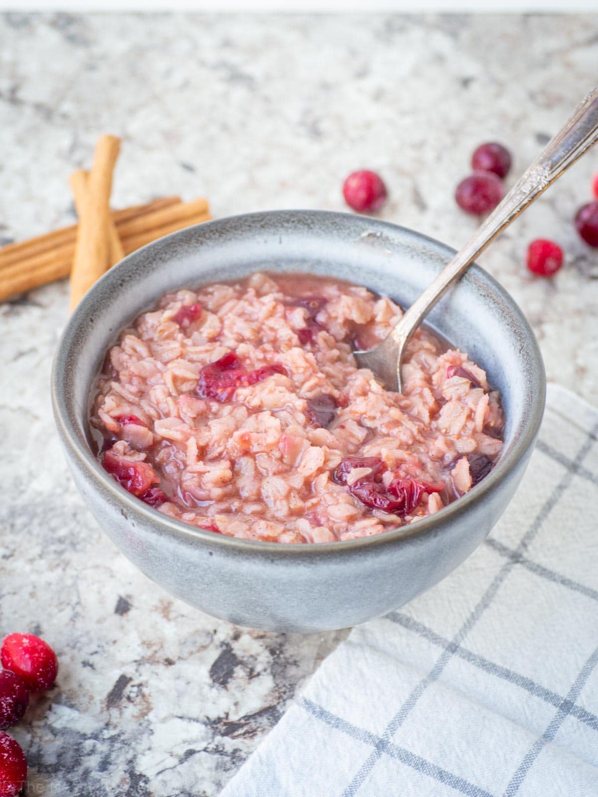 Pink oatmeal in a bowl with cranberries on the countertop.