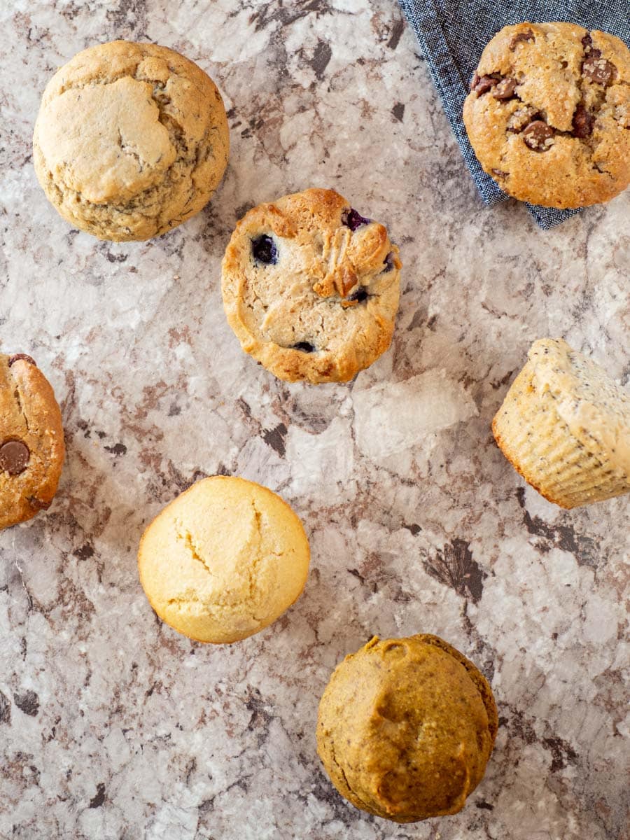 Different flavors of oat flour muffins spread out on a countertop.