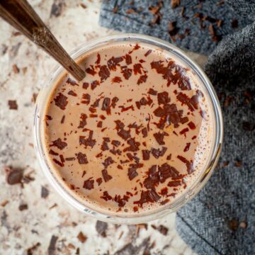 Hot chocolate in a cup with a spoon garnished with chocolate shavings.