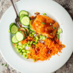 Salmon in a bowl with rice, cucumber, carrots and edamame.