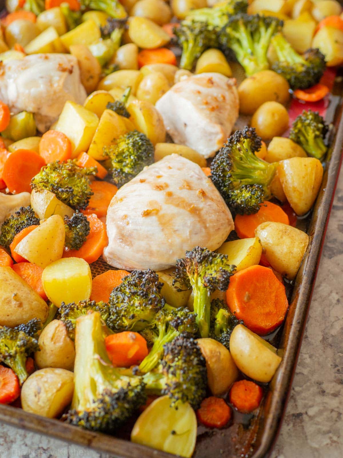 Chicken on a sheet pan with vegetables and topped with honey garlic sauce.