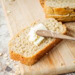Piece of oat flour bread being buttered.